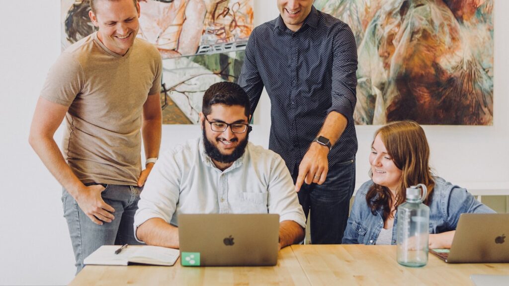 four coworkers smiling around laptop at table