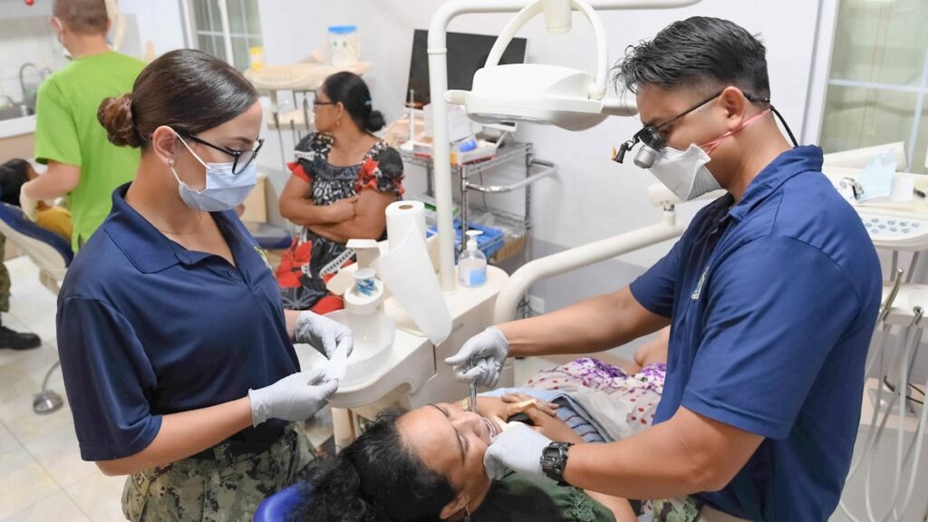 Dentists examine a patient's teeth in a clinic.