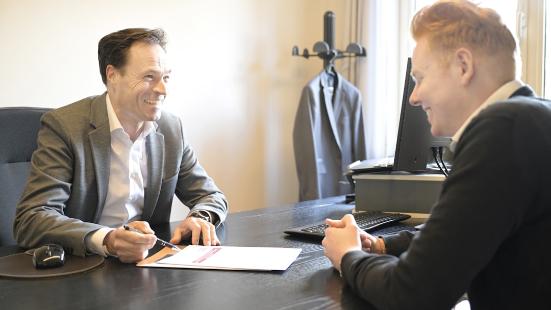 Two smiling men discussing documents at an office desk.