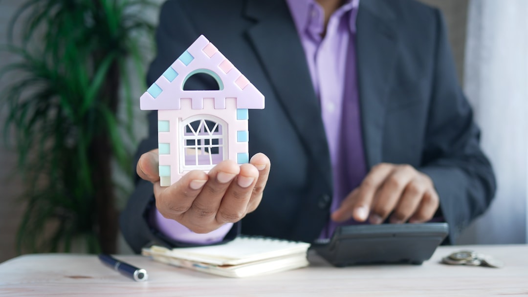 man holding model house at desk with calculator