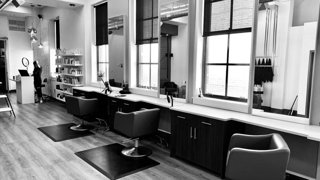 grayscale photo of woman using laptop near three salon chairs