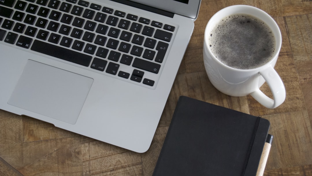 macbook pro beside white ceramic mug on brown wooden table